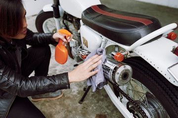 Concentrated biker wearing leather jacket using rag and cleaning spray in order to wipe dirt from his motorcycle