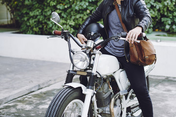 Obraz na płótnie Canvas Stylish man wearing leather jacket holding helmet in hand while sitting on vintage motorcycle ready for twisted adventures