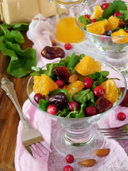 Fruit salad with orange pieces, cranberries, date fruits and arugula in a glass salad bowl