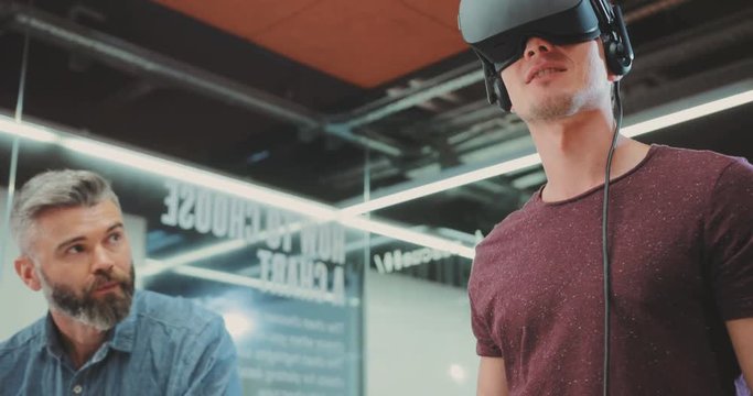 One man in virtual reality glasses, the second man uses a laptop in the office. Contemporary design. Shot on RED Epic Camera.
