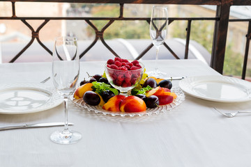 Plate of fruit with raspberries, grapes and plums is on the table for two