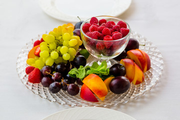 Plate of fruit with raspberries, grapes and plums is on the table for two