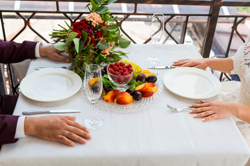 Bride and groom sitting at a table on which there is a plate of fruit.