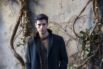 Handsome young man leaning against tree in autumn, wearing black coat