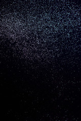Blue glitter, on a dark, black backdrop. Vertical photography.