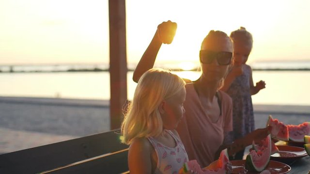 Mother with blonde babies eat watermelon sunset beach rapid slow motion 
