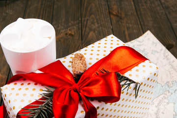 Cup of hot chocolate with marshmallows stands before red present box on white map