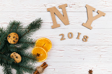 Wooden letters 'NY 2018' lie on the floor surrounded with cookies, fir branches, spices and oranges