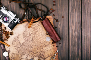 Old yellow map, glasses, coins, leather case, camera, watch, compasses, coffee beans, other spices and cookies lie on wooden floor