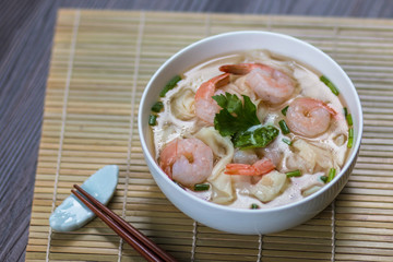 Shrimp wonton noodle soup with braised pork in soup on wooden table - Asian food style.