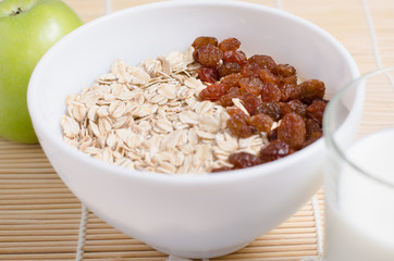Oatmeal with raisins on the tablecloth from bamboo. Milk, green Apple