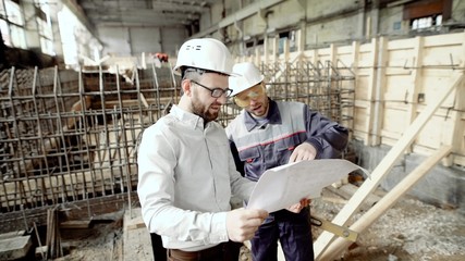 Architect and chief foreman at the construction site of the plant. Men discuss drawbacks in the drawing. Against the background of construction work.