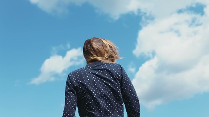Beautiful young woman girl blue shirt sky clouds back view portrait nowhere wind blowing long hair creative shoot windy weather turning around smiling happy pretty lady summer sunny day fun cheerful