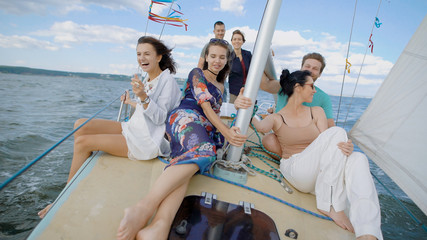 A company of friends ride on a yacht on the high seas or the ocean, buddies sit on deck and enjoy a light wind that blows their hair and clothes