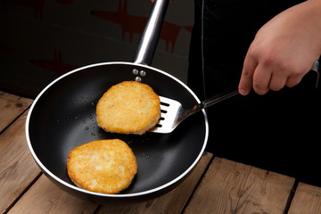 simple dish of Russian, Belarusian, Ukrainian cuisine on a old wooden boards, the cook fries the potato pancakes in the frying pan