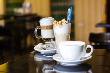 Three different coffee cups and on darck caffee background. Cappuccino, latte and frappe on table