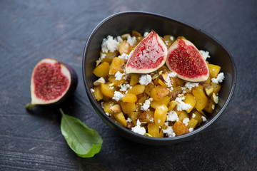 Salad with roasted pumpkin, cheese, pistachios and ripe figs on a dark stone background, studio shot