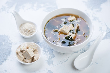 White tableware with miso soup, tofu cheese and sesame on a white concrete background