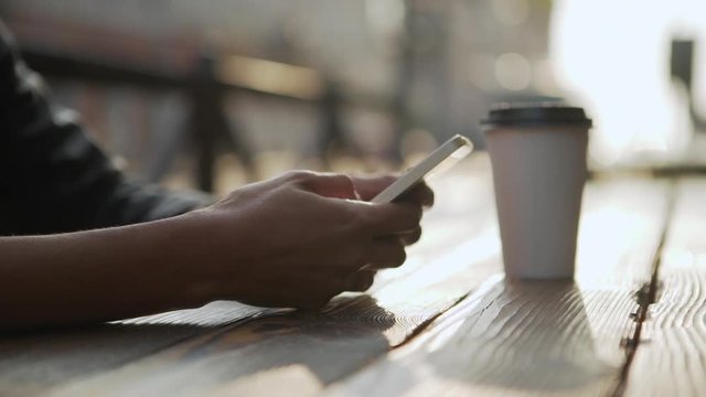 female metis hands holding using smartphone while sitting in city cafe typing having takeaway coffe reading news scrolling with defocused background slow motion