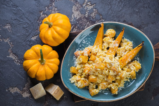 Risotto with pumpkin served in a turquoise plate, flat-lay on a brown stone background