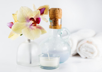 Aroma oil, orchid and candle on white table. Blurred towels in background. Healthy lifestyle, spa
