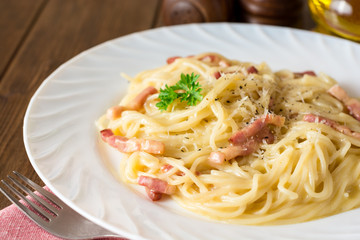 Classic pasta carbonara. Spaghetti with bacon, egg yolk and parmesan cheese on white plate on dark wooden background.