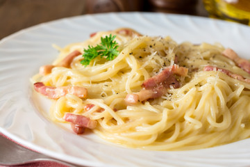 Classic pasta carbonara. Spaghetti with bacon, egg yolk and parmesan cheese on white plate on dark wooden background.