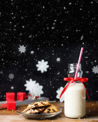 Vintage bottle of milk with red ribbon and santas cookies on wooden table over black background. Text space