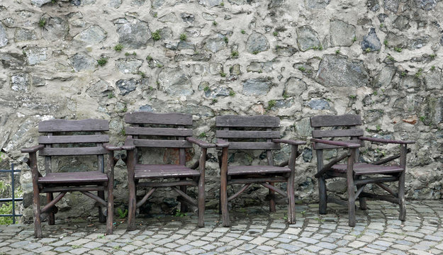 Vier rustikale braune Holzstühle vor einer alten Steinmauer