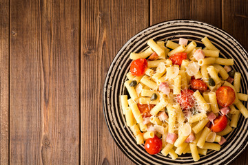 Pasta with bacon, garlic, tomatoes, capers and parmesan cheese in plate on dark wooden background.