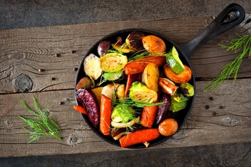 Cast iron skillet of roasted autumn vegetables against a rustic dark background
