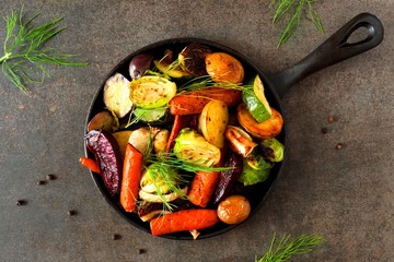 Cast iron skillet of roasted autumn vegetables, above view over a dark stone background
