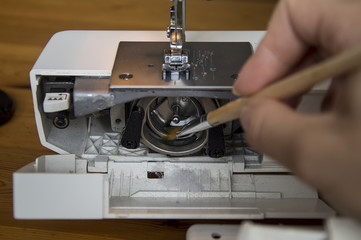 cleaning and preparation of sewing machine.A woman uses a brush to clean the inside of the sewing machine from dust