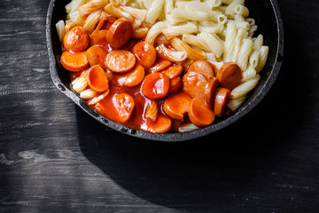 Pasta with sausages and tomato sauce on a black background