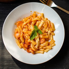 Pasta with sausages and tomato sauce on a black background