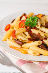 Penne pasta with mushrooms, bell pepper, chilli and parsley on white plate on white wooden background.