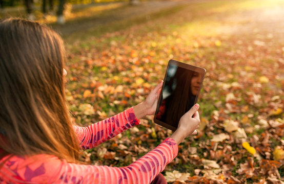 young girl taking picture digital tablet pc in autumn park