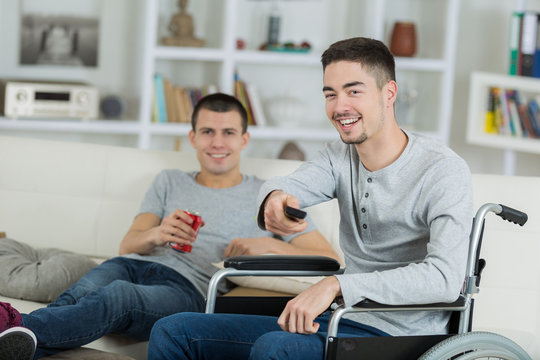 cheerful disabled young man watching tv with friend