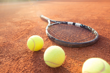 Close up view of tennis racket and balls on the clay tennis court, recreational sport (color toned image)