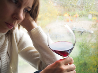Lady in a depression with a glass of wine by the window.

