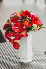 A bouquet of different red flowers in a vase on a table. Close-up. Artwork
