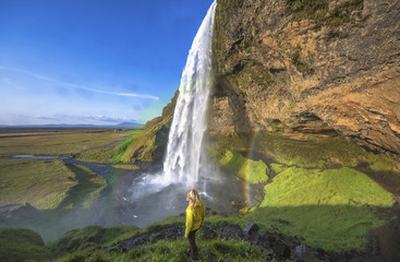 Woman under Seljalandsfoss waterfall, Iceland. Sunny day in Iceland with rainbow