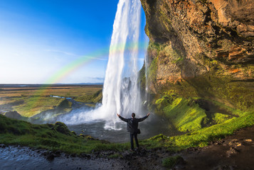 Tourist standing in front of Seljalandsfoss one of the best known waterfalls in southern Iceland, Seljalandsfoss , Iceland