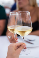 Female hands toasting with glasses of white wine, closeup