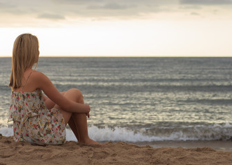 Fototapeta na wymiar Young woman sitting on sand and looking to a sea. Travel vacations concept.