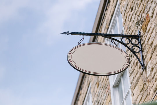 Blank sign hanging from a wrought iron bracket above a shop