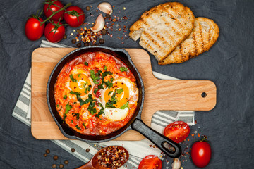 Breakfast. Shakshuka with bread in pan on a black rustic background. Fried eggs with tomatoes. Top view. Space for text. Middle eastern style breakfast or lunch