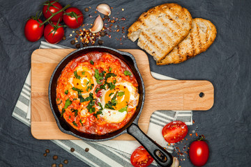 Breakfast. Shakshuka with bread in pan on a black rustic background. Fried eggs with tomatoes. Top view. Space for text. Middle eastern style breakfast or lunch