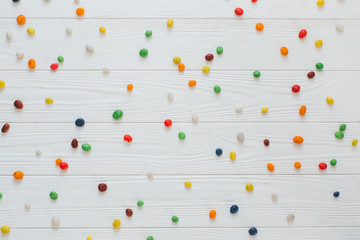 Many multicolored sweet candies on white wooden background.