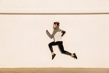 Full length photo of young fitness woman in sport wear jumping near white wall